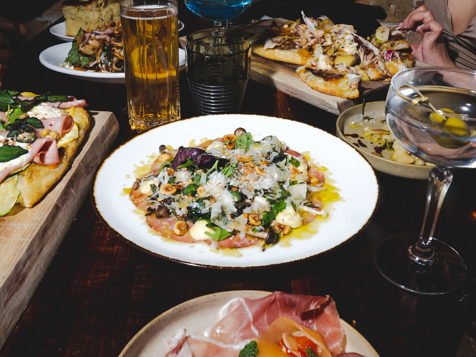 A shared Notte table with pizza, salumi, cocktails, and wine
